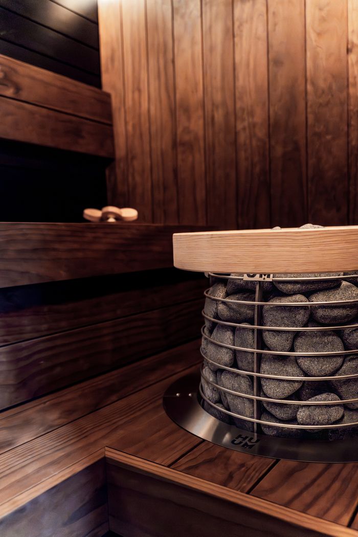services-04 Elegant modern sauna interior featuring a Nordic design with a stone heater and wooden benches.