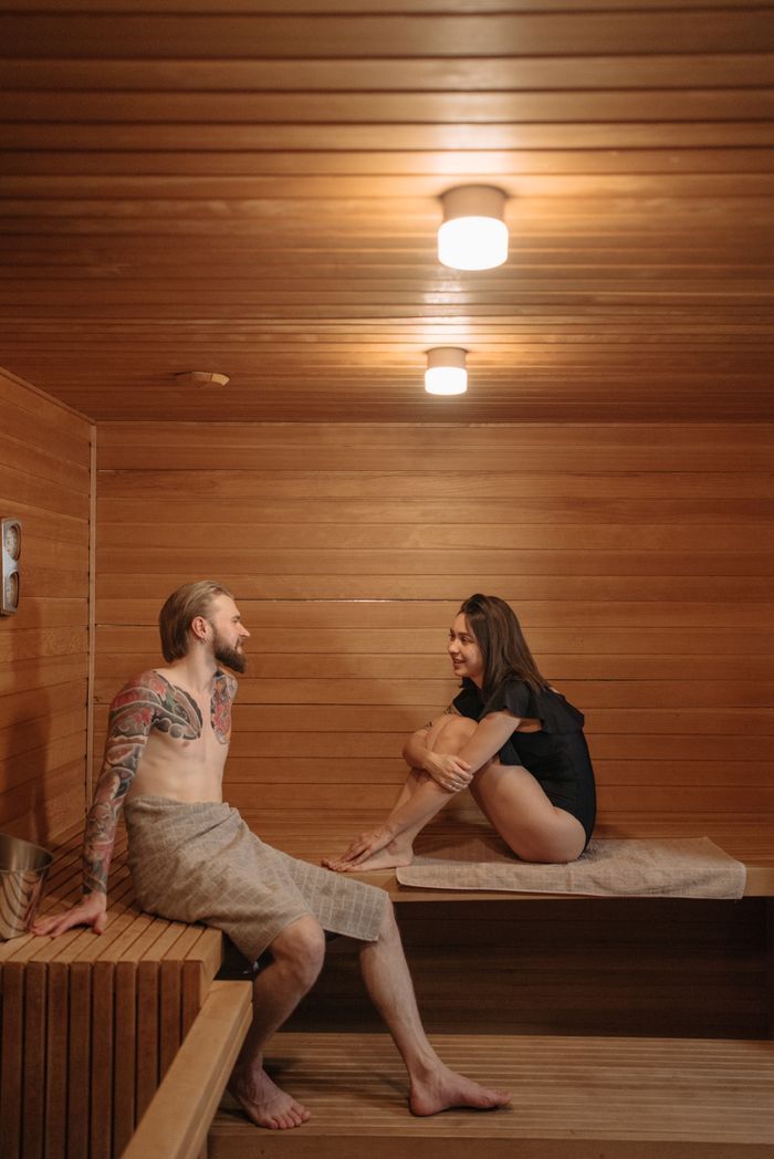 services-03 A couple relaxing and talking inside a wooden sauna room, enjoying their sauna session.